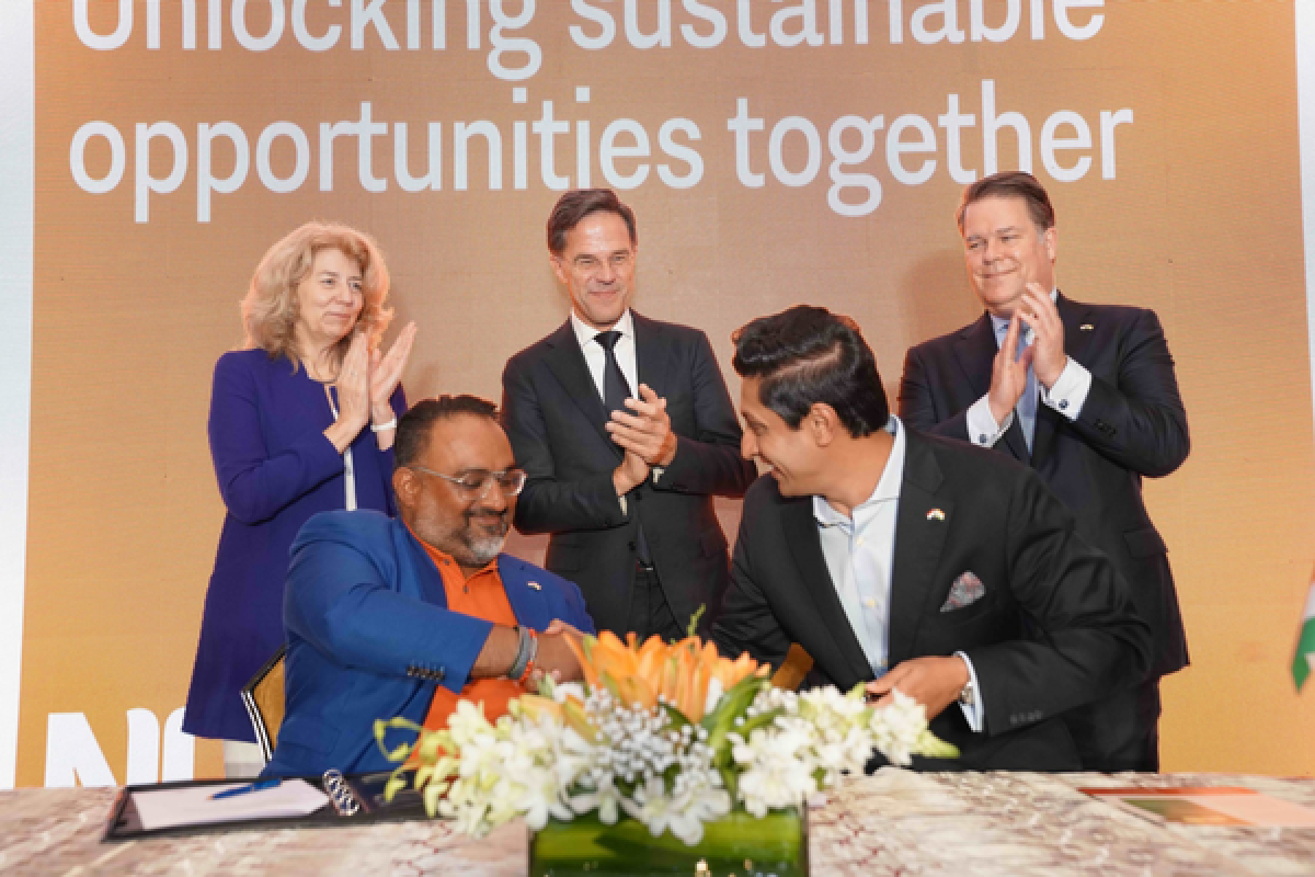 two PIB members shake hands at a table whilst ex Prime Minister Mark Rutte and two others applaud them from behind