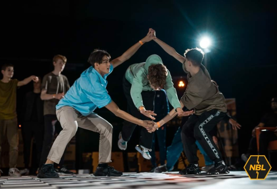 breakdancer jumps through hands of other breakdancers 
