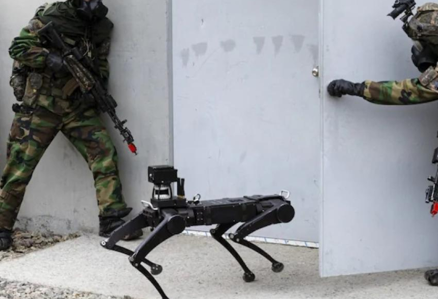 two men in combat gear holding rifles stand next to a robot combat dog 